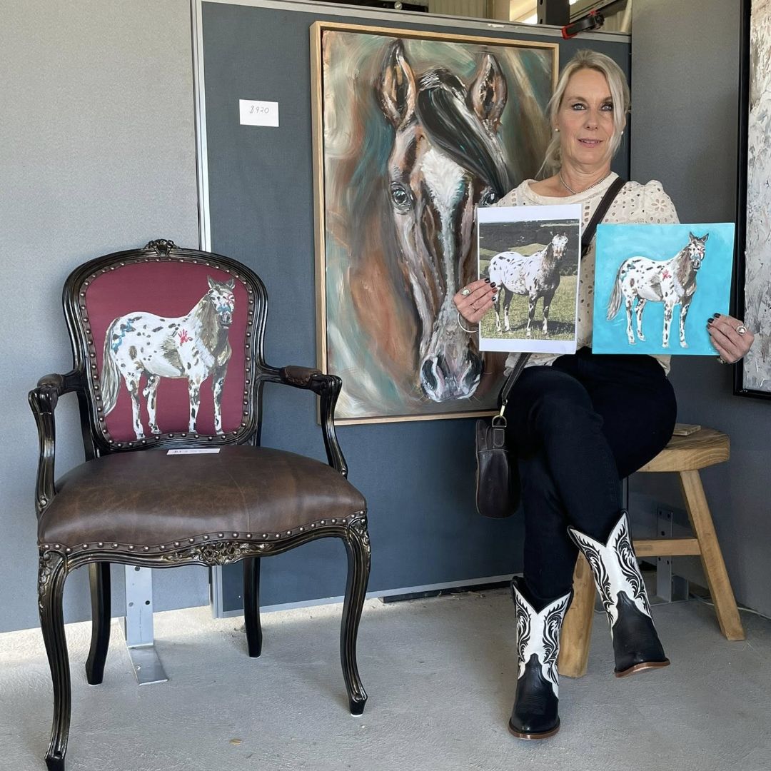 Artist Nicolee holding horse-themed artworks in an art gallery setting